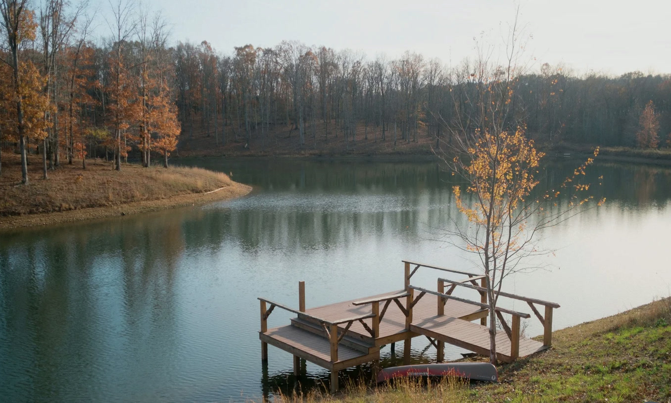Wooden benches on a deck overlooking a still lake framed by autumn woods